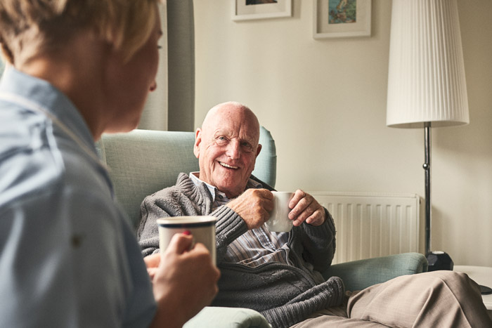 elderly man smiling at care giver while drinking coffee